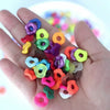 A hand holds an assortment of colorful acrylic spacer beads in various shapes and sizes.