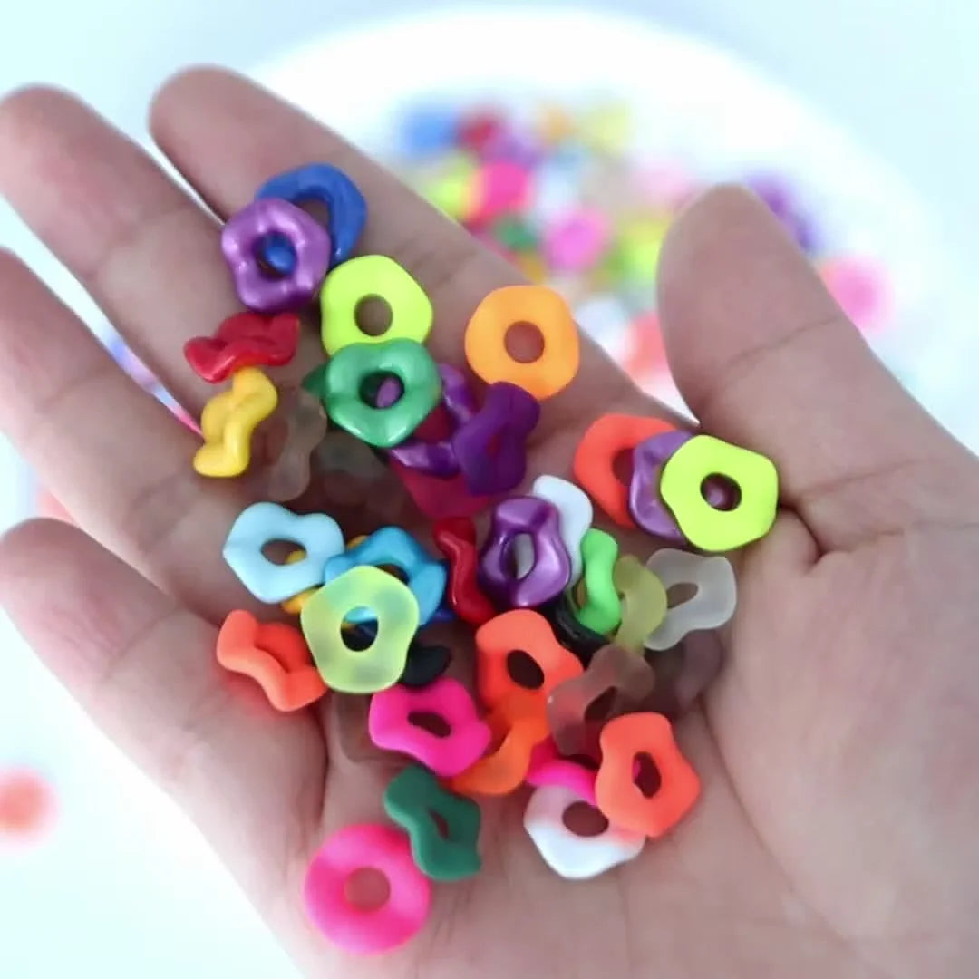 A hand holds an assortment of colorful acrylic spacer beads in various shapes and sizes.
