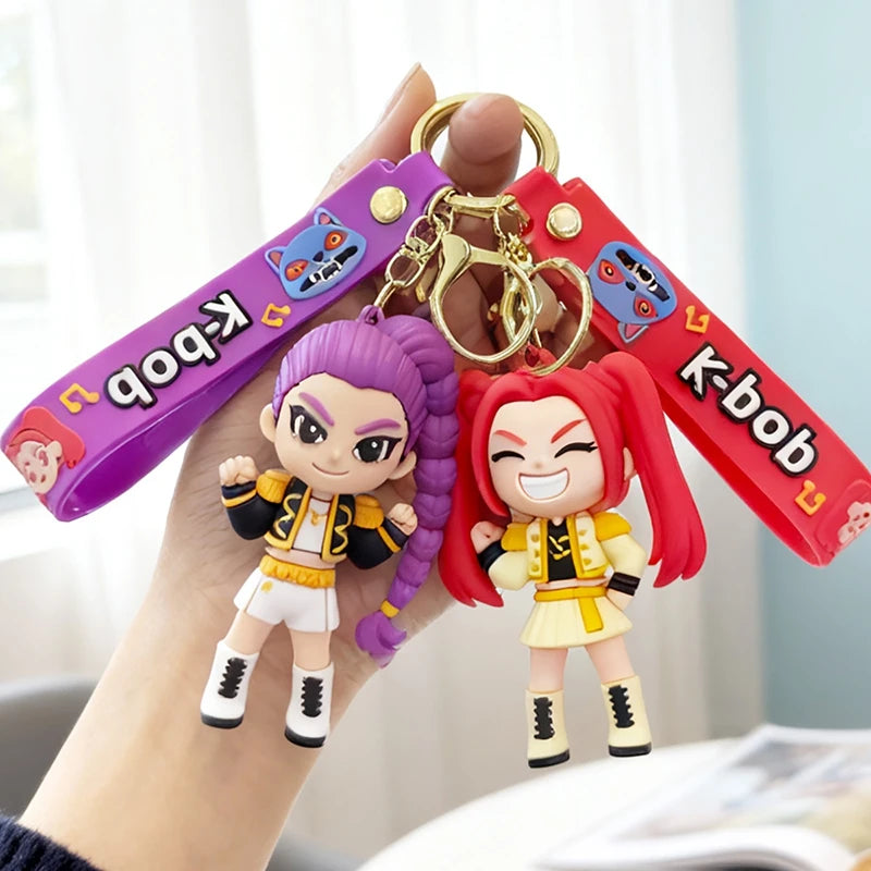 A hand holds a Kpop Rumi keychain charm featuring two figures, one purple-haired and one red-haired.