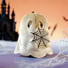A white ghost-like figure with black spiderwebs is displayed on a surface against an orange background.