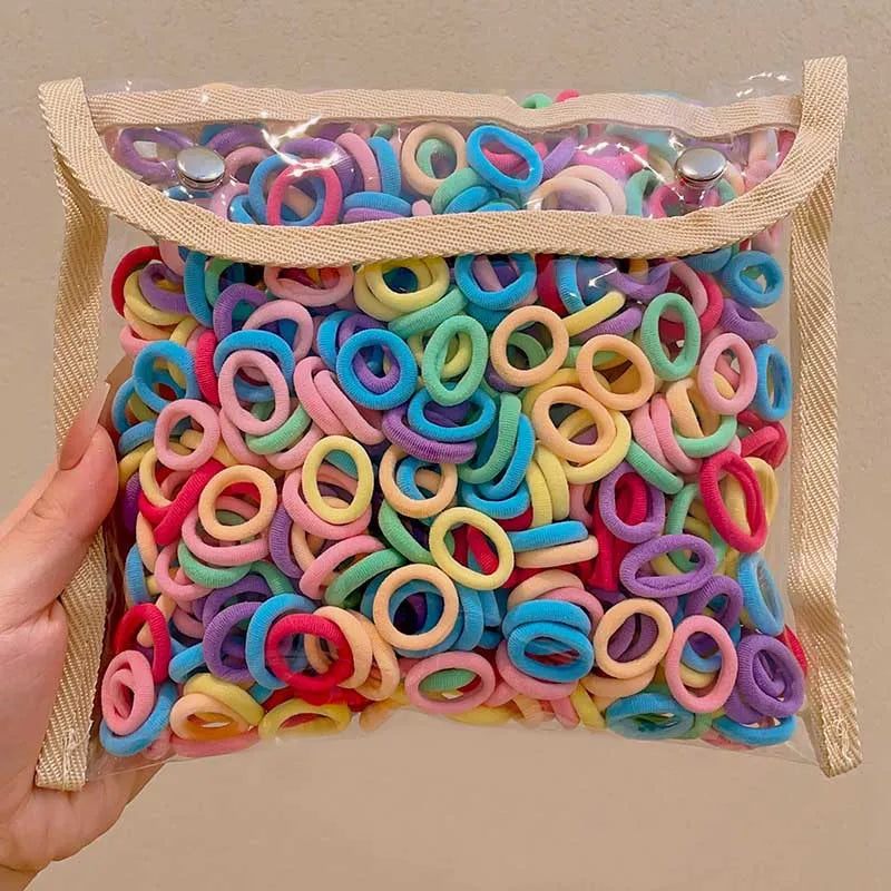 A hand holds a clear plastic bag filled with a multi-pack of colorful nylon hair ties in various colors.