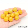 A hand holds several smooth, yellow agate crystal spheres.