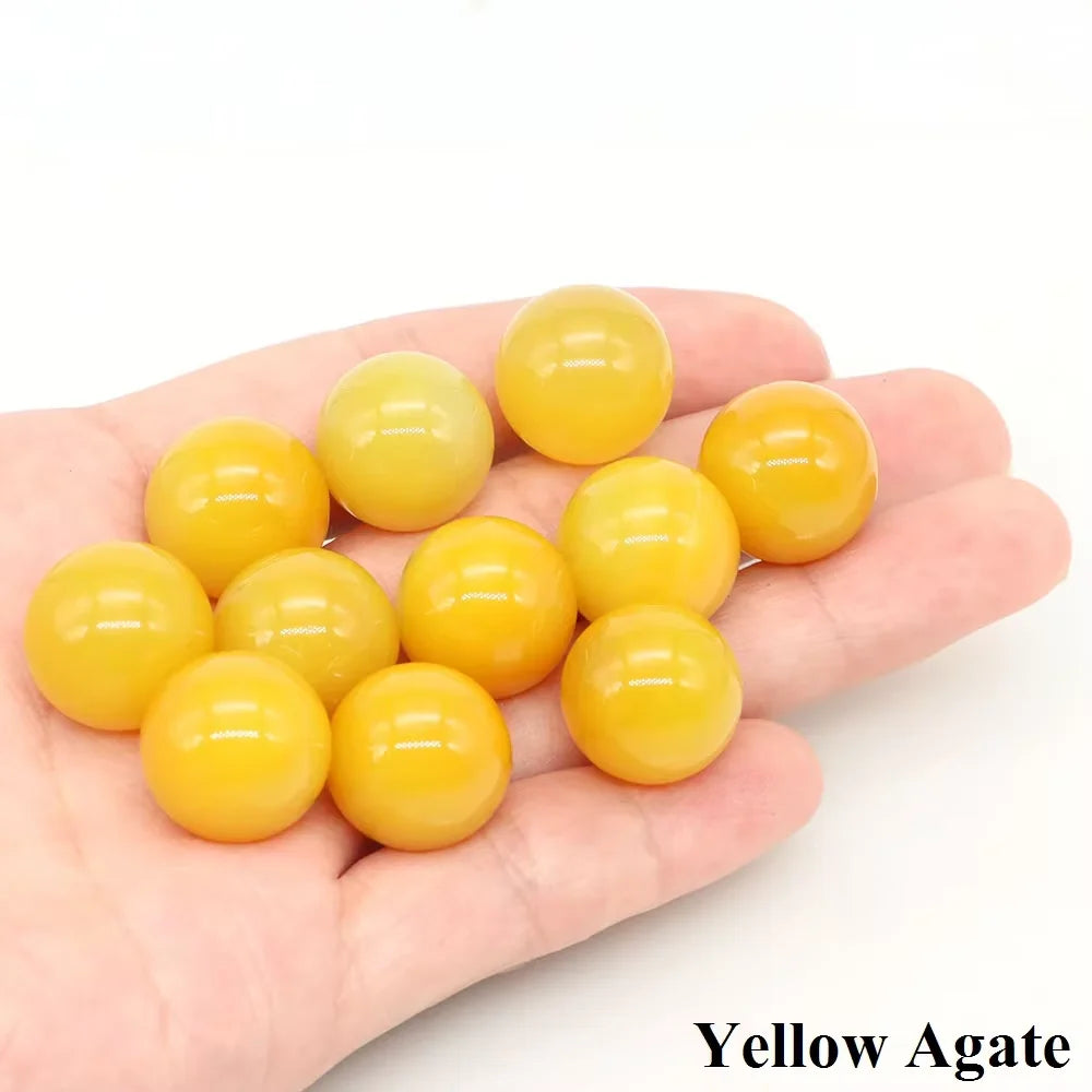 A hand holds several smooth, yellow agate crystal spheres.