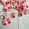 Pink crochet mini pig keychains arranged on a white lace background with a ruler.