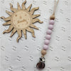 A wooden sun-shaped bead pacifier clip with a string of light purple beads and a silicone teether.