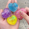 A hand holds four heart-shaped squishy toys in various colors including blue, purple, pink, and yellow.