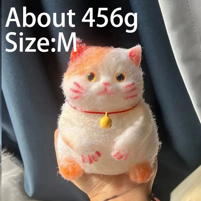 A small, fluffy orange and white cat-shaped squishy toy with a red collar being held in a hand.