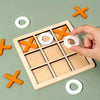 A wooden tic tac toe board game with orange and white pieces is being held by a hand on a green surface.