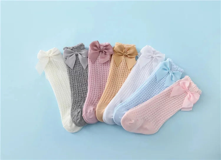 A collection of baby girl lace knee socks in various pastel colors and shades with bows arranged on a light blue background.