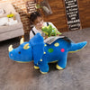 A large blue dinosaur plush toy lying on a gray floor in a room with brick walls and a woman wearing glasses.