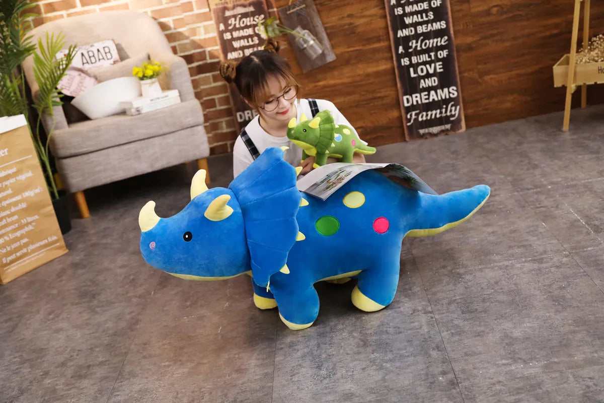 A large blue dinosaur plush toy lying on a gray floor in a room with brick walls and a woman wearing glasses.
