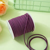 A roll of purple velvet faux suede braided ribbon for crafting and gift wrapping, resting on a light green surface.