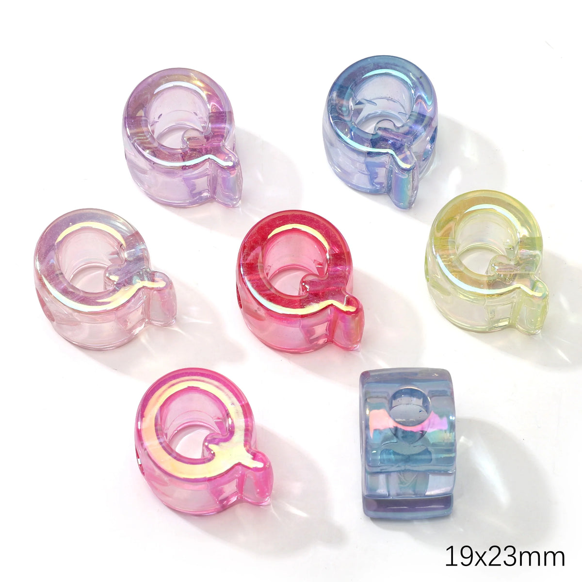 A collection of colorful acrylic alphabet beads in various shades of purple, pink, and clear are displayed on a white backgro