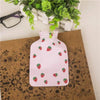 A pink portable hot water bottle with a cozy cover featuring a pattern of strawberries, resting on a brown textured surface.