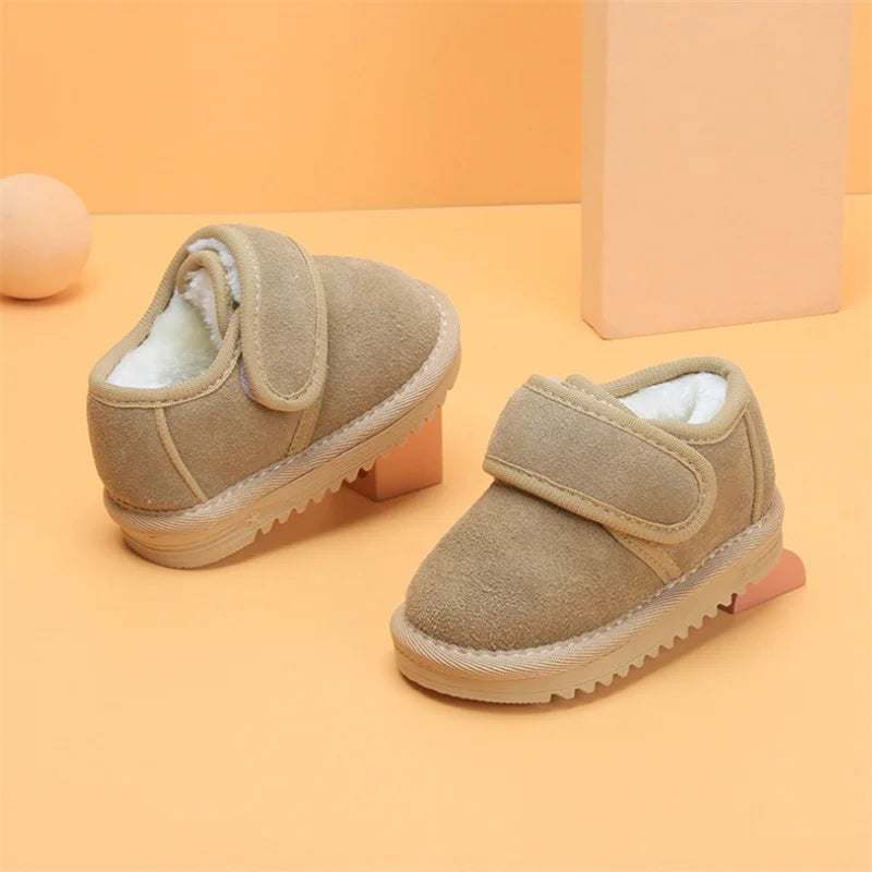 A pair of tan faux leather winter boots for toddlers with a shearling lining and rubber sole, displayed on an orange backgrou