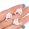 Pink and white enamel dolphin charms for jewelry making displayed on a hand.