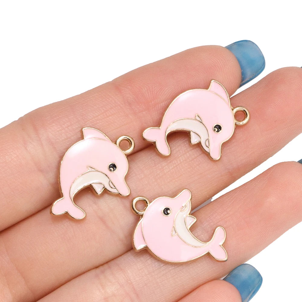 Pink and white enamel dolphin charms for jewelry making displayed on a hand.