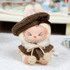 A cute doll wearing a brown tweed beret and matching cape set with fluffy white trim.