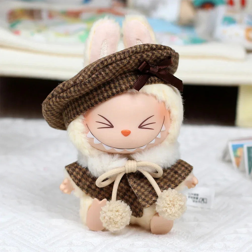 A cute doll wearing a brown tweed beret and matching cape set with fluffy white trim.