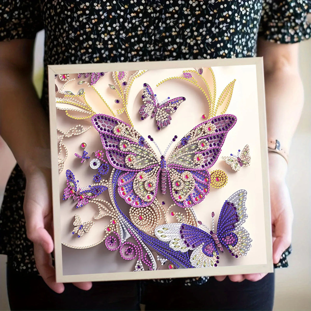 A hand holds a DIY diamond painting kit featuring sparkling purple and silver butterfly art on a clear background.