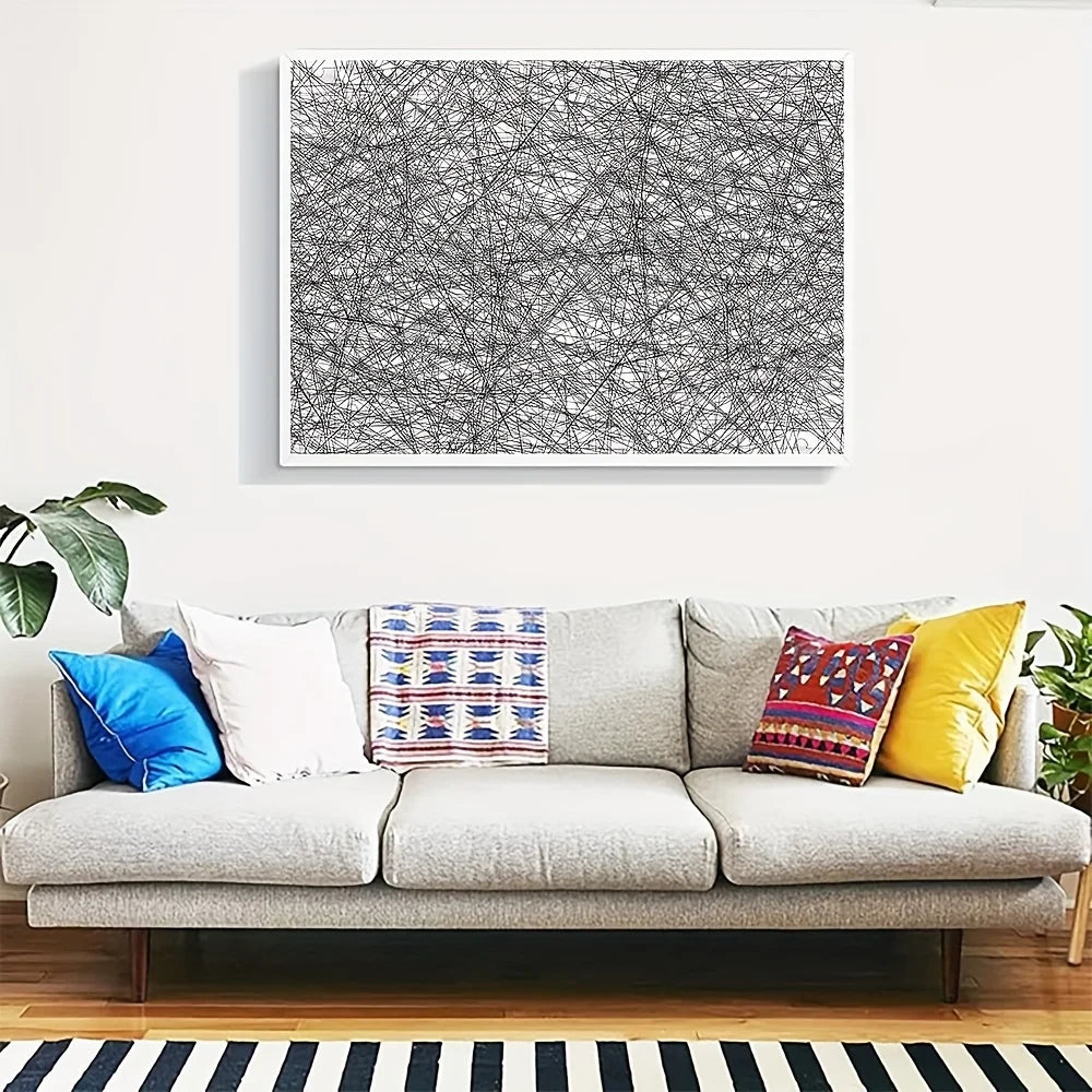 A framed black and white abstract line art jigsaw puzzle hanging on a white wall above a gray sofa.