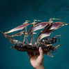 A hand holds a detailed steampunk pirate ship 3D wooden puzzle model kit against a dark teal background.