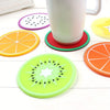A set of colorful fruit pattern PVC coasters, including orange, lime green, and purple designs, displayed around a white mug.