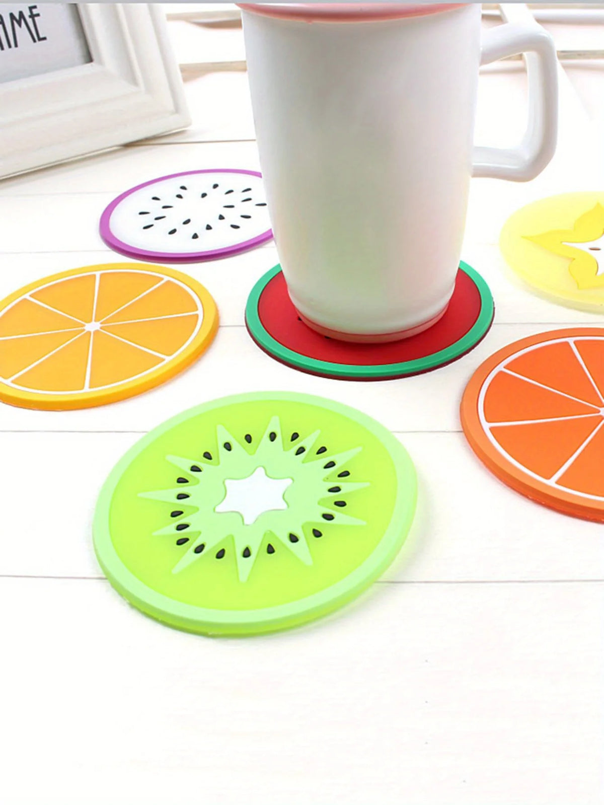 A set of colorful fruit pattern PVC coasters, including orange, lime green, and purple designs, displayed around a white mug.