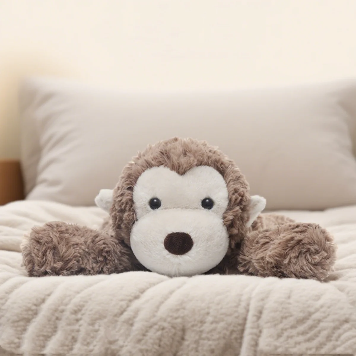 A fluffy brown monkey plush toy resting on a light beige blanket.