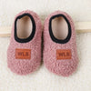 Pair of pink fuzzy baby slippers with black anti-slip soles resting on a light background.