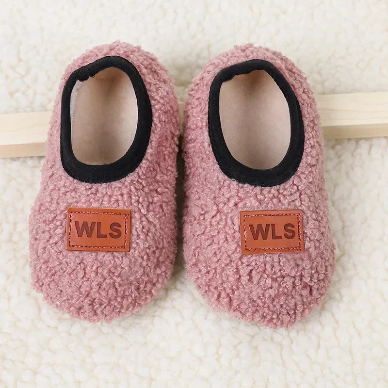 Pair of pink fuzzy baby slippers with black anti-slip soles resting on a light background.