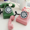 A pink vintage rotary telephone piggy bank with a green telephone and receiver next to it.