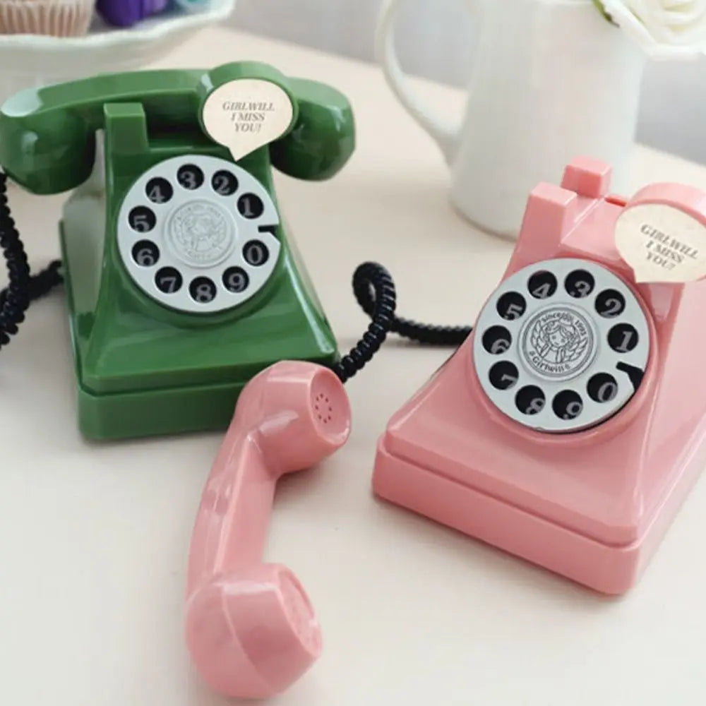 A pink vintage rotary telephone piggy bank with a green telephone and receiver next to it.