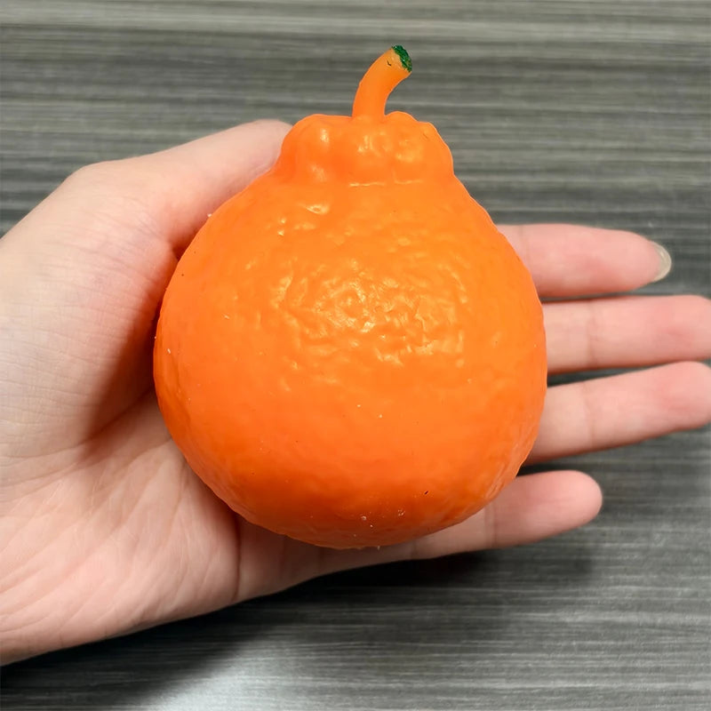 An orange squishy stress relief toy shaped like a small pumpkin is held in a person's hand.