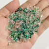 A handful of tumbled stone chips in shades of pink and green are held in a hand.