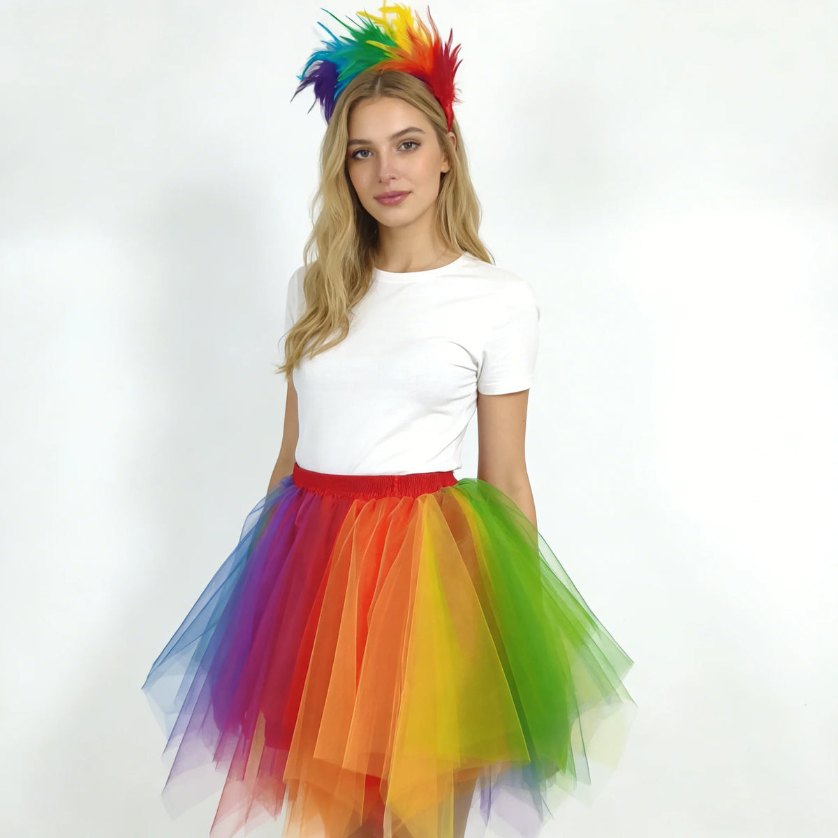 A young woman wearing a white top and a colorful rainbow tulle tutu skirt and a matching feather headband.