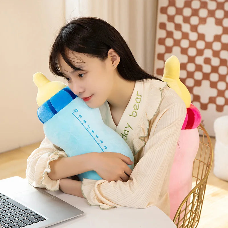A young woman is holding a light blue milk bottle plush pillow with yellow accents, resting it on a white table.