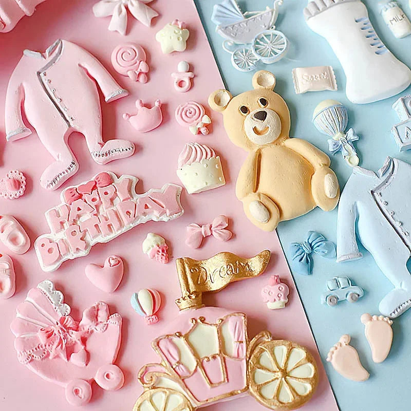 A collection of pink and white silicone baby-themed cake molds including a stroller, bottle, pacifier, teddy bear, and variou