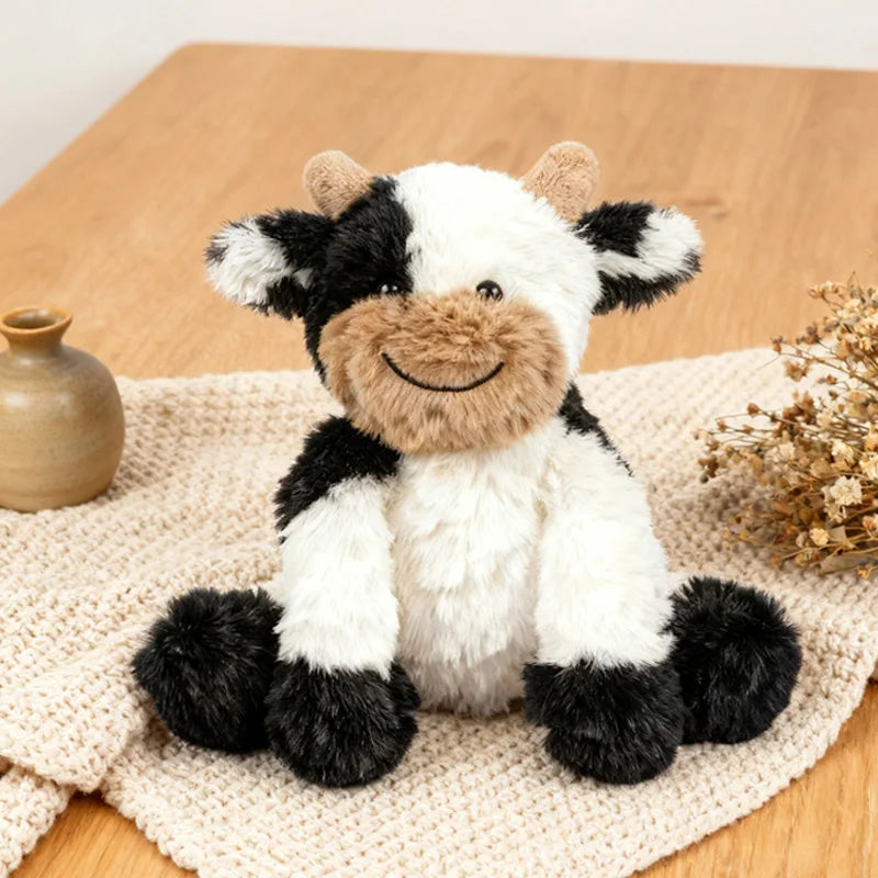 A super soft sitting cow plush toy with black and white markings resting on a beige woven fabric.