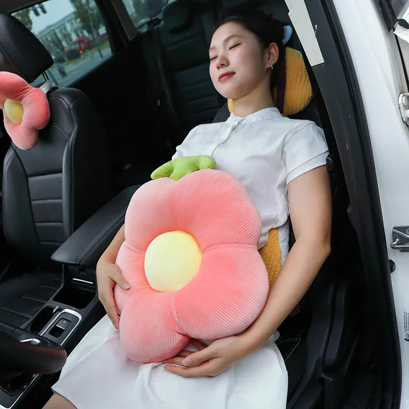 A woman is sitting in a car and holding a large pink flower-shaped plush pillow with yellow accents.
