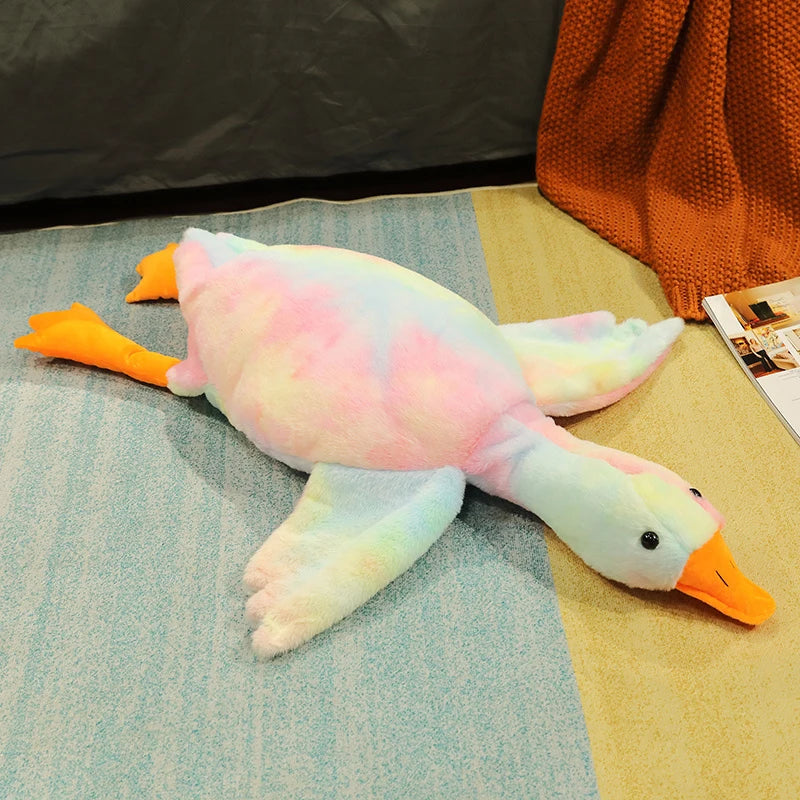 An extra-large plush goose pillow with pink and yellow feathers lying on a light blue surface.
