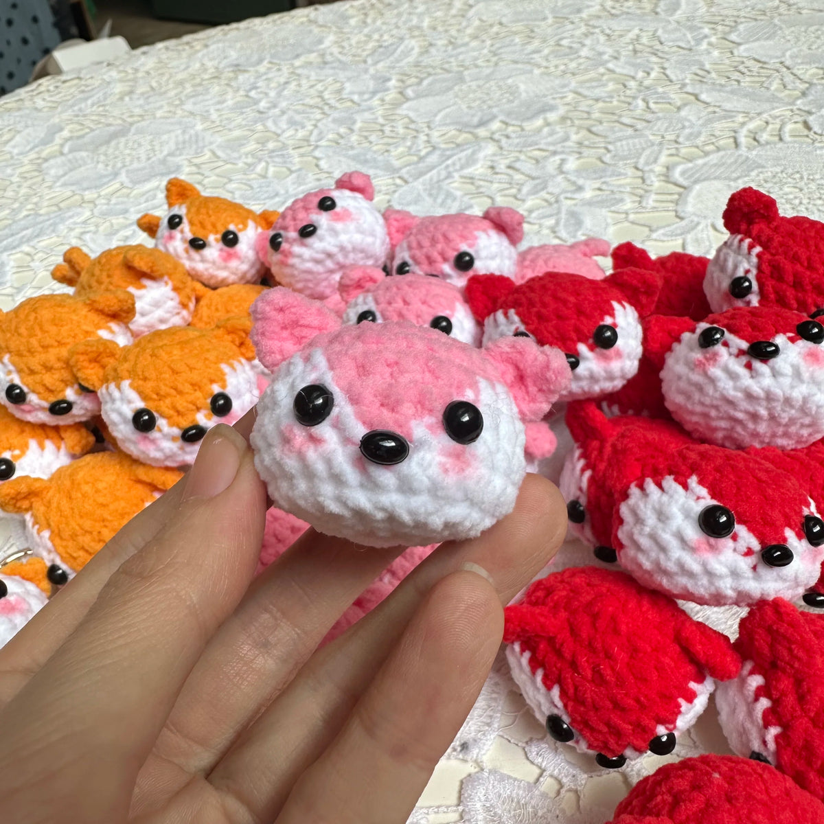A hand holds a collection of handcrafted crochet animal keychains in various colors including orange, pink, and red.