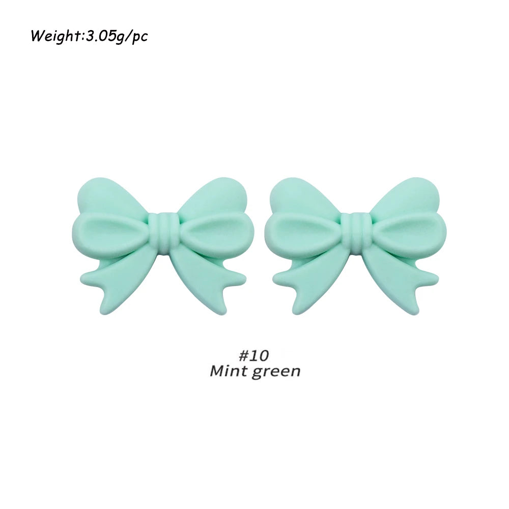 A pair of mint green silicone bow tie beads for jewelry making and craft projects.