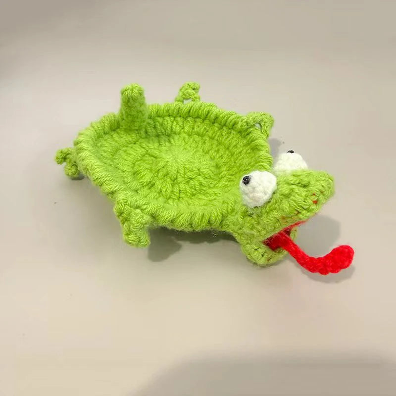 Handmade crochet lizard coaster with green body, white eyes, and red tongue.