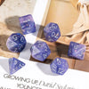 A set of purple glitter resin polyhedral dice scattered on a light surface with a brown paper background.