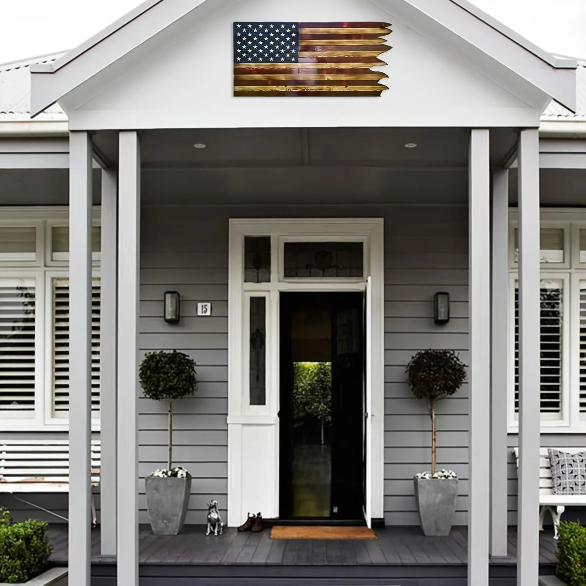 A wooden American wavy flag hangs above a front door on a gray house facade.