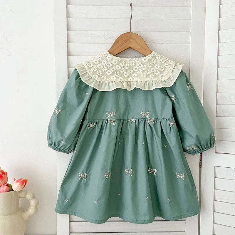 A mint green girls' party dress with lace collar and embroidered details hanging on a wooden hanger.