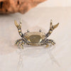 A brass crab figurine statue with detailed claws and body, resting on a reflective surface.