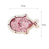 A wooden busy board shaped like a fish, decorated with pink and red sequins, featuring castle and bulldozer themes.