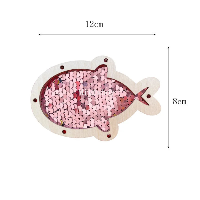 A wooden busy board shaped like a fish, decorated with pink and red sequins, featuring castle and bulldozer themes.